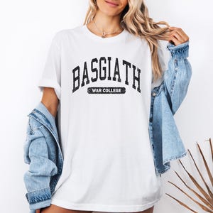 Op de afbeelding: Wit T-shirt met een zwarte afbeelding met de tekst "Basgiath War College" in een vintage universitaire lettertype.