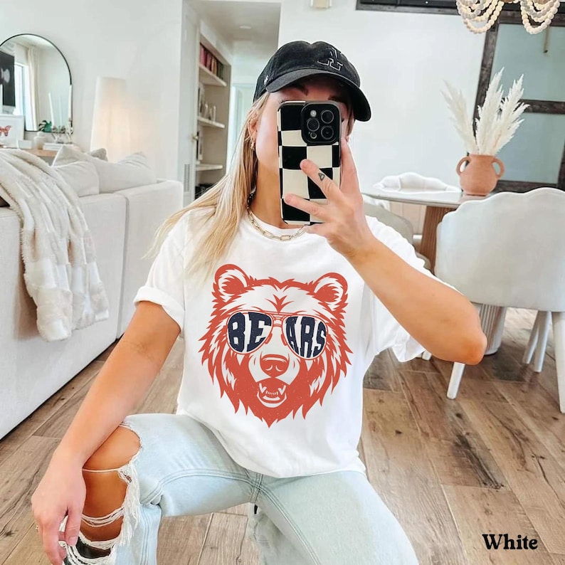 Pu&ograve; includere: Maglietta bianca con un orso rosso che indossa occhiali da sole blu con la scritta "BEARS" sulle lenti. L'orso indossa occhiali da sole.