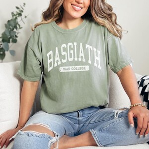 Op de afbeelding: Een groen T-shirt met de tekst "BASGIATH WAR COLLEGE" in wit op de voorkant.