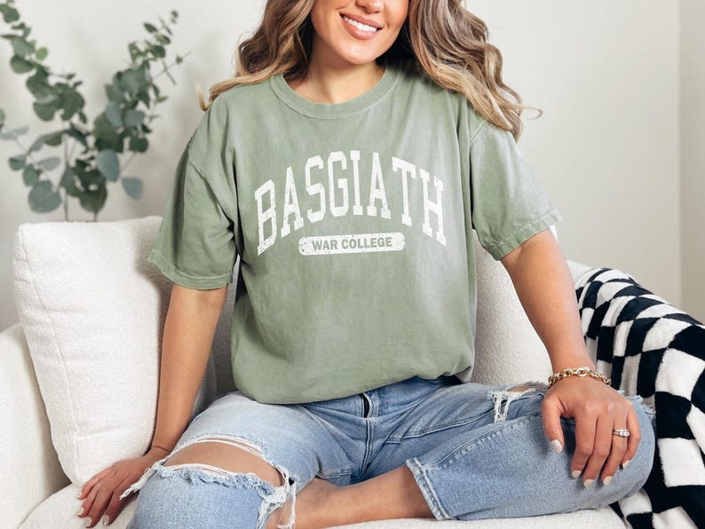 Op de afbeelding: Een groen T-shirt met de tekst "BASGIATH WAR COLLEGE" in wit op de voorkant.