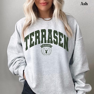 May include: A grey sweatshirt with the text "TERRASEN GALATHYNIUS" in green lettering and a green stag logo. The sweatshirt has a crew neck and long sleeves.