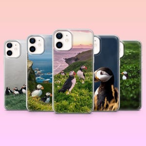 Puede incluir: Cinco fundas para teléfono que muestran imágenes de frailecillos en su hábitat natural. Las fundas presentan diversas escenas, incluyendo frailecillos en laderas cubiertas de hierba, cerca del mar y retratos en primer plano. Las fundas son transparentes con un acabado brillante.