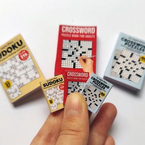 K&ouml;nnte beinhalten: Miniatur-Sudoku- und Kreuzwortr&auml;tselb&uuml;cher in Gelb, Rot und Blau. Die Sudoku-B&uuml;cher zeigen die Zahl 316, w&auml;hrend die Kreuzwortr&auml;tselb&uuml;cher die Zahl 80 anzeigen. Kleine Puzzle-B&uuml;cher.
