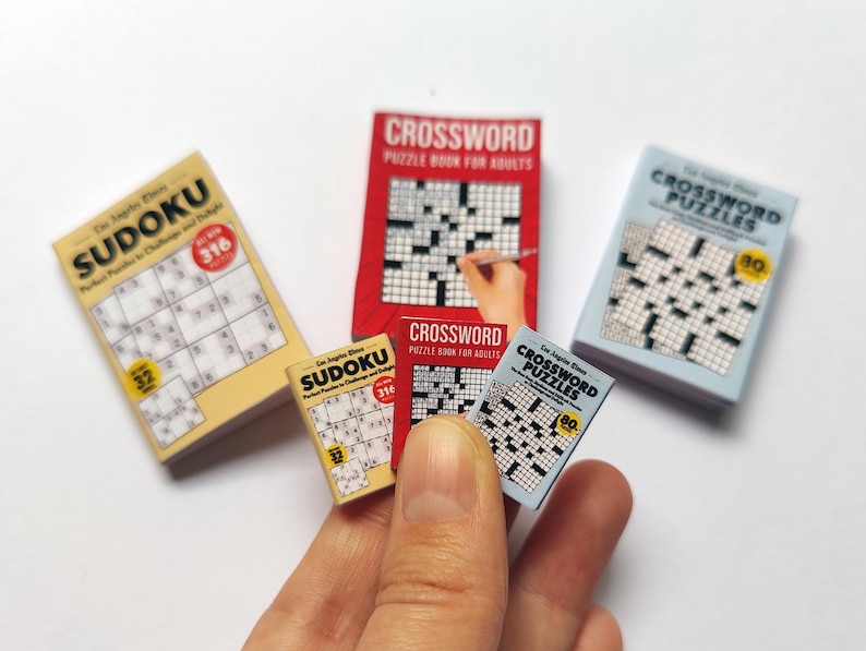 K&ouml;nnte beinhalten: Miniatur-Sudoku- und Kreuzwortr&auml;tselb&uuml;cher in Gelb, Rot und Blau. Die Sudoku-B&uuml;cher zeigen die Zahl 316, w&auml;hrend die Kreuzwortr&auml;tselb&uuml;cher die Zahl 80 anzeigen. Kleine Puzzle-B&uuml;cher.