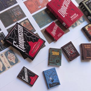 May include: A collection of miniature books featuring classic literature titles. The books have various colors and designs, including red, black, and blue covers. Titles include "Frankenstein," "Dracula," and "The Legend of Sleepy Hollow."