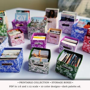 May include: A collection of miniature storage boxes in various colors, filled with tiny magazines and books. The boxes feature a leaf pattern and are arranged on a white surface. The text on the magazines is visible, including "THE ENGLISH GARDEN" and "CROSSWORD".