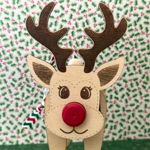 May include: Wooden reindeer ornament with a red nose and brown antlers. The reindeer is standing on a green background with a snowflake pattern.