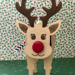May include: Wooden reindeer ornament with a red bottle cap nose, brown antlers, and a red and white striped ribbon.