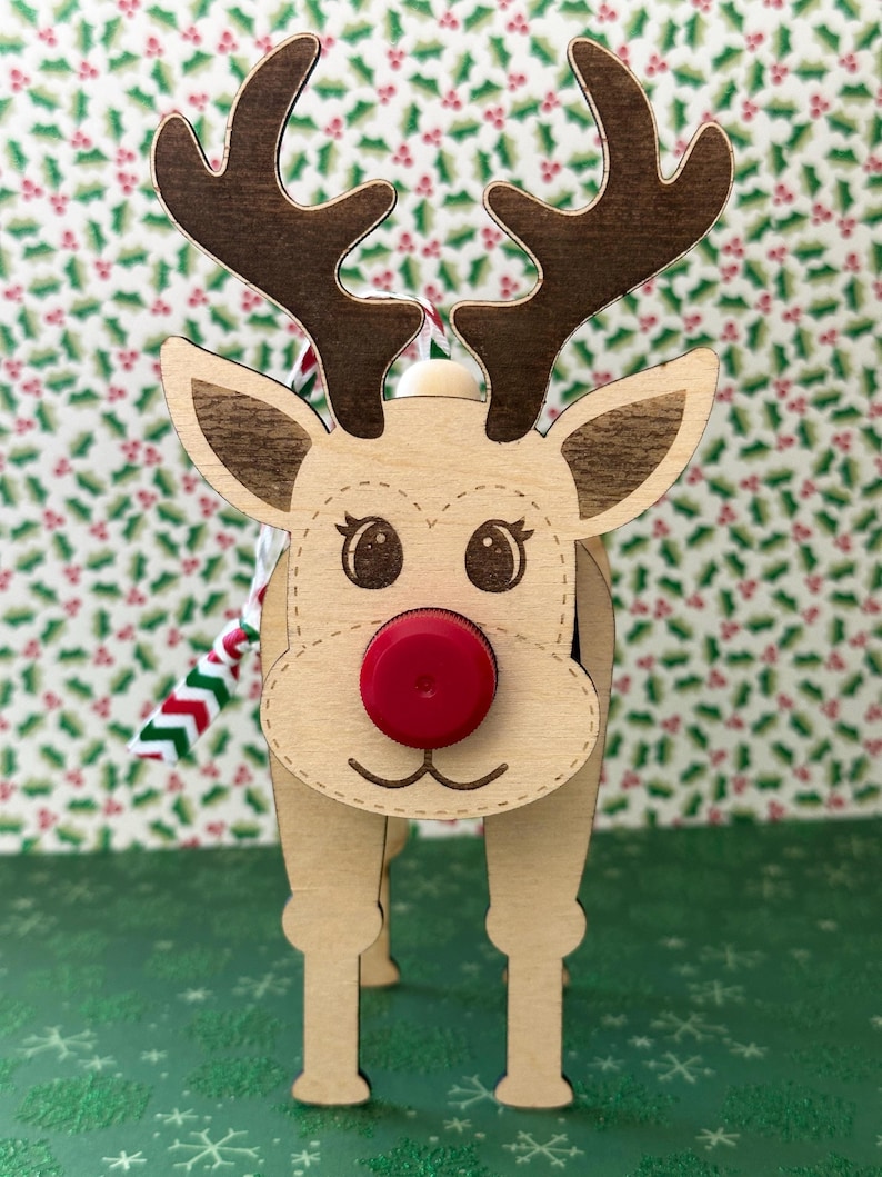 May include: Wooden reindeer ornament with a red nose and brown antlers. The reindeer is standing on a green background with a snowflake pattern.