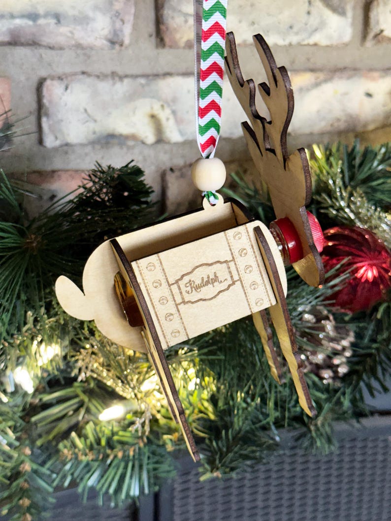 May include: Wooden reindeer Christmas ornament with a red and green striped ribbon, a wooden bead, and the word "Rudolph" engraved on the side.