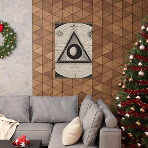 May include: A framed print featuring a celestial design with a triangle, moon, stars, and suns. The artwork is in black and white, with intricate line details. The print is displayed on a wooden wall above a gray sofa, with a Christmas tree and wreath in the background.