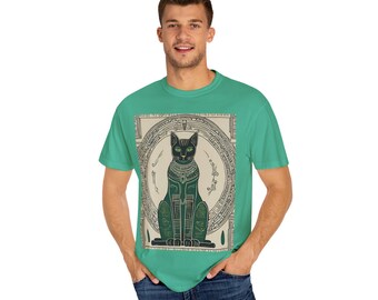 May include: A teal t-shirt featuring a graphic of a stylized, seated black cat with green eyes and gold accents, set within a circular frame. The design has an ancient Egyptian aesthetic.