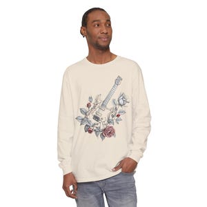 May include: Cream-colored long-sleeve shirt featuring a detailed illustration of an electric guitar surrounded by roses and leaves in shades of gray, pink, and blue. The shirt is made of a soft, comfortable material.