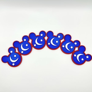May include: A set of blue, red, and white Mickey Mouse-shaped coasters. Each coaster features a crescent moon and star design. The coasters are arranged in a curved pattern against a white background.