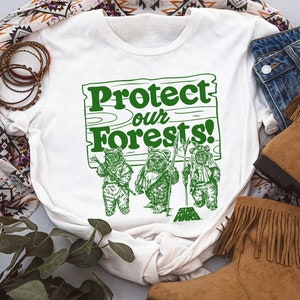 May include: White t-shirt with a green graphic of a wooden sign that says "Protect our Forests!" with three Ewoks from Star Wars standing in front of it.