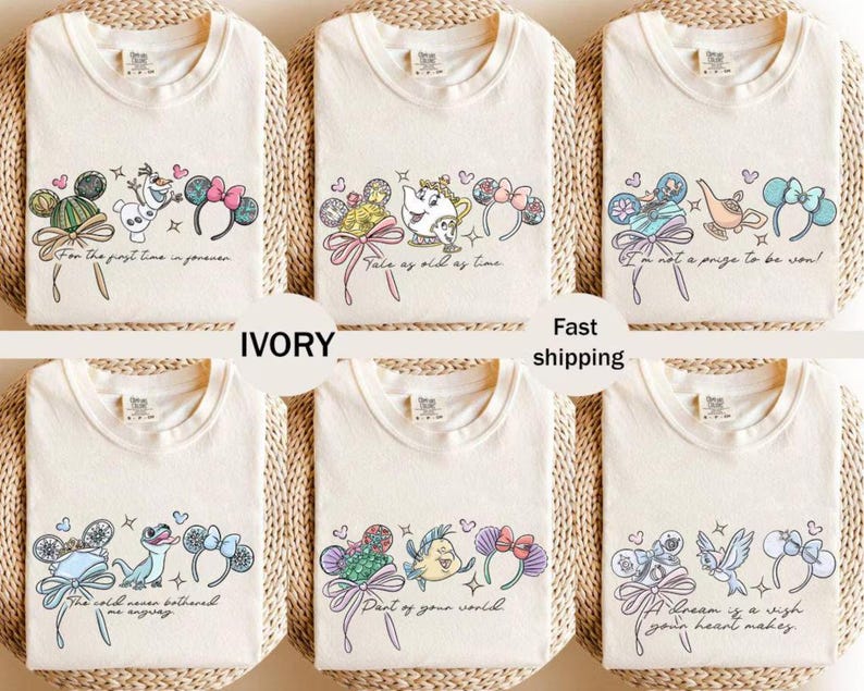 May include: Ivory t-shirts with Disney character designs. Each shirt has a different graphic featuring characters, bows, and phrases such as "Tale as old as time" and "Part of your world". The shirts are arranged on a woven surface.