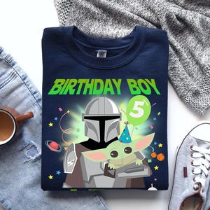 May include: Navy blue t-shirt with a graphic featuring The Mandalorian and Grogu, the text "BIRTHDAY BOY" in green, and a number 5 balloon. The design includes stars and confetti.