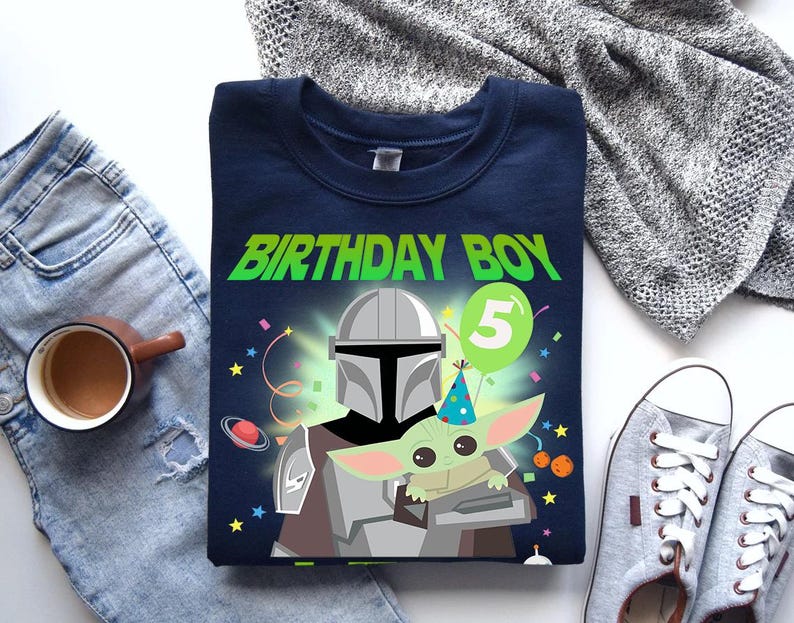 May include: Navy blue t-shirt with a graphic featuring The Mandalorian and Grogu, the text "BIRTHDAY BOY" in green, and a number 5 balloon. The design includes stars and confetti.