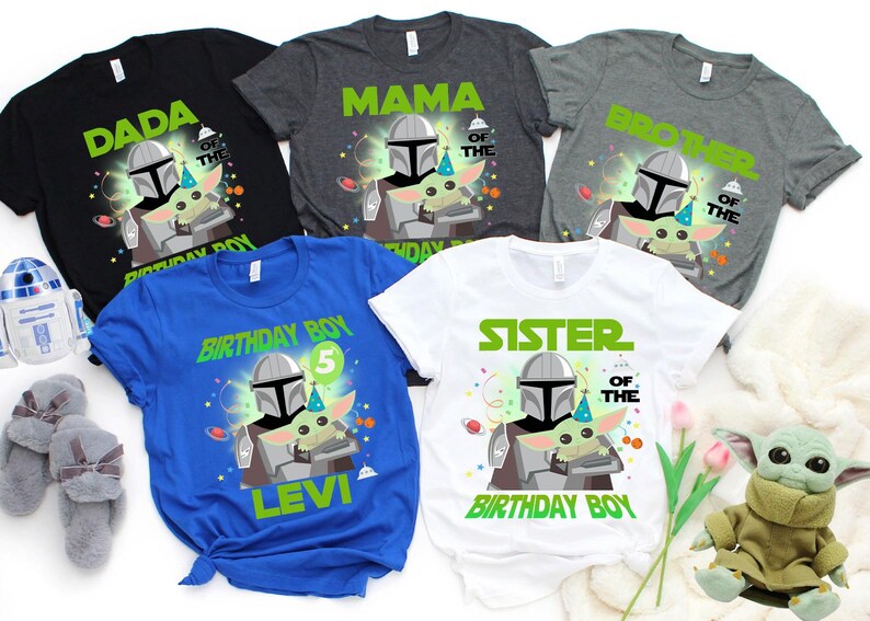 May include: A collection of t-shirts with a Star Wars theme. The shirts are black, gray, blue, and white, each featuring a graphic of The Mandalorian and Grogu. Text includes "DADA", "MAMA", "BROTHER", "BIRTHDAY BOY", and "SISTER".