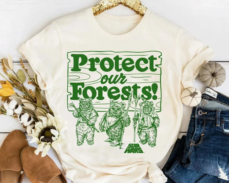 May include: A white t-shirt with a green graphic of three Ewoks from Star Wars standing in front of a sign that says "Protect our Forests!"
