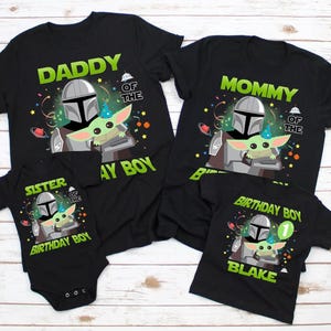 May include: Black t-shirts with a Star Wars theme, featuring the Mandalorian and Grogu. The shirts are labeled "Daddy", "Mommy", "Sister", and "Birthday Boy", with the name "Blake" on one. Festive birthday decorations are included.