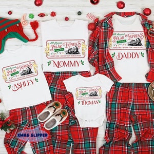 May include: A set of four white t-shirts with a red and green plaid pattern. The shirts feature a vintage-style ticket design with the words "All Aboard Polar Express" and the names "Ashley", "Mommy", "Daddy", and "Thomas".
