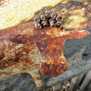 May include: A rusty metal sculpture of a cow with a curly metal head. The sculpture is painted white with brown rust spots.