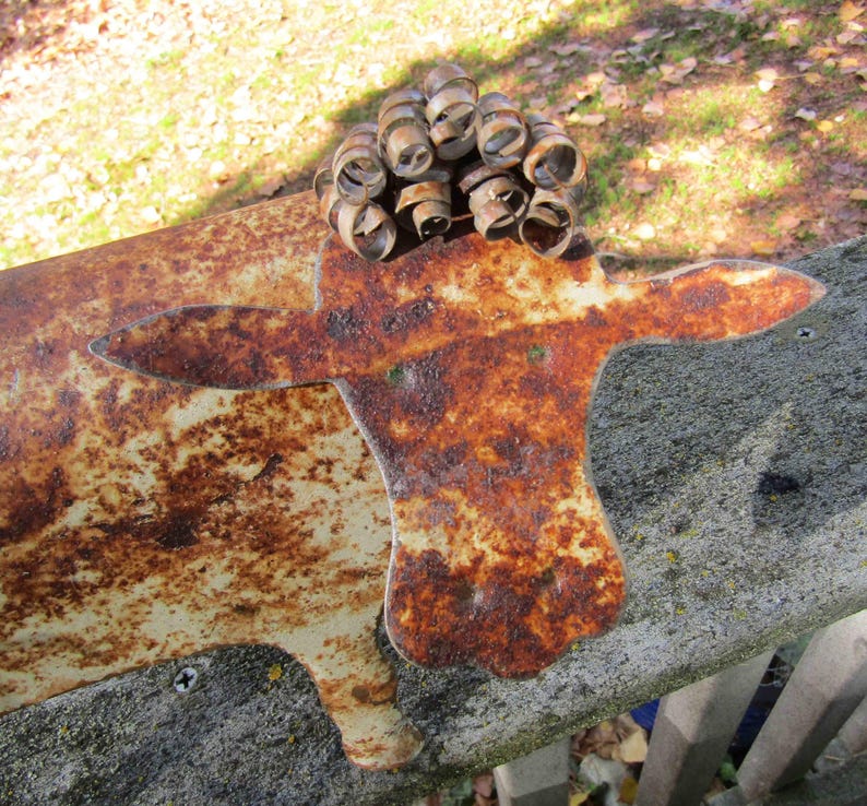 May include: A rusty metal sculpture of a cow with a curly metal head. The sculpture is painted white with brown rust spots.