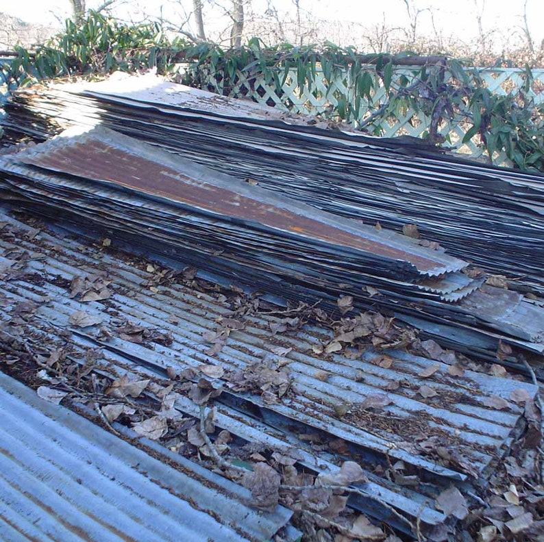 May include: A stack of corrugated metal sheets, weathered and rusted, with some leaves and debris on top.