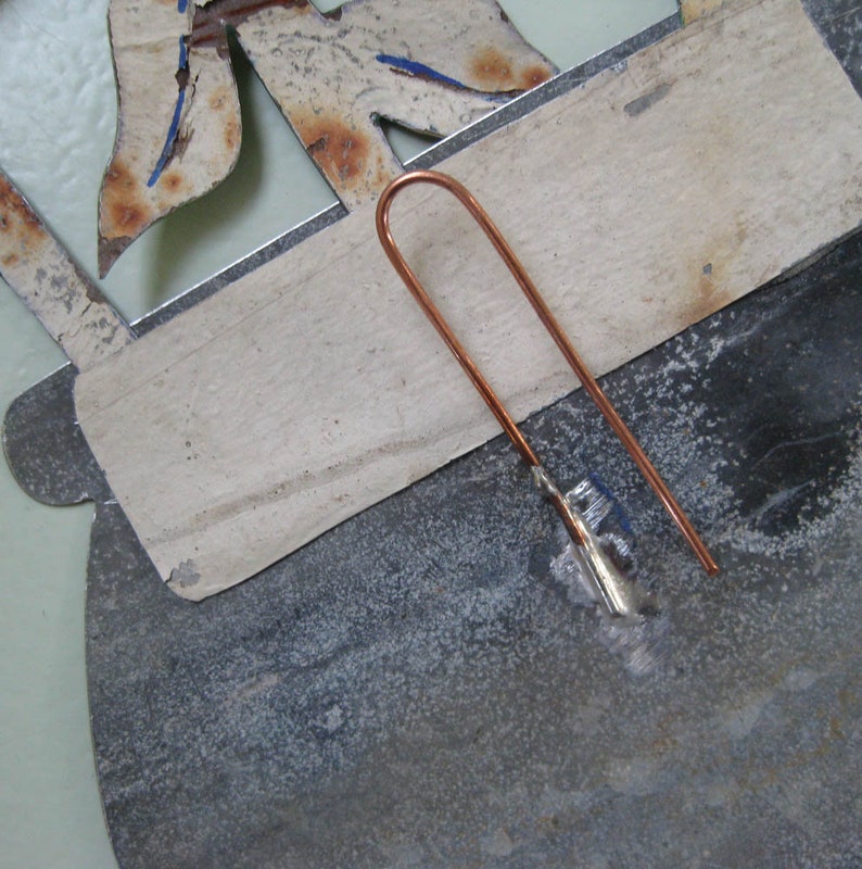 May include: A close-up of a metal object with a copper wire attached to it. The wire is bent into a loop and appears to be soldered to the metal.