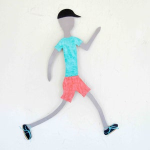 Può includere: Un ritaglio di carta di una persona che indossa un berretto nero, una camicia turchese e pantaloncini rossi. La persona sta correndo con le braccia distese e le gambe piegate alle ginocchia.