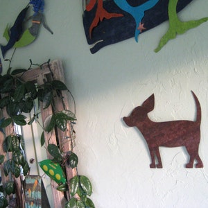 May include: A brown metal silhouette of a chihuahua dog mounted on a light green wall. The dog is facing right and has its ears perked up. There are other decorative items on the wall, including a blue and green whale and a green and blue mermaid.