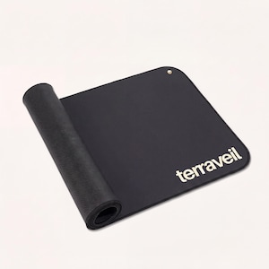 Könnte beinhalten: Eine schwarze Yogamatte mit dem Markennamen "terraveil" in Weiß aufgedruckt. Die Matte ist teilweise aufgerollt und zeigt eine strukturierte Unterseite. Eine kleine Metallöse ist am oberen Rand sichtbar.