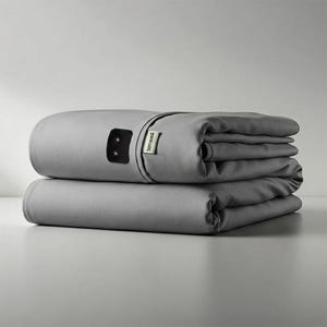 Può includere: Due coperte grigie piegate sono impilate l'una sull'altra. La coperta superiore ha un pannello di controllo nero e una piccola etichetta con la scritta "terraveil". Le coperte sono realizzate in un materiale morbido e liscio.