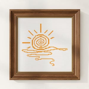 Könnte beinhalten: Ein quadratischer Holzrahmen mit einer Kreuzstichstickerei auf weißem Stoff. Das Motiv zeigt eine orangefarbene Sonne mit spiralförmiger Mitte und strahlenden Strahlen über horizontalen orangefarbenen Linien, die Wasserreflexionen darstellen.