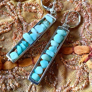May include: A pair of silver earrings with a rectangular frame filled with light blue aquamarine stones.