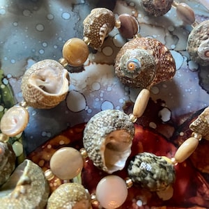 May include: A close-up of a necklace made of seashells and wooden beads. The shells are a variety of colours and shapes, and the beads are a light brown colour.