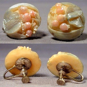 May include: A pair of vintage clip-on earrings. Each earring features a carved, off-white floral design with pink accents. The earrings have a screw-back closure and are marked "MADE IN" on the back.