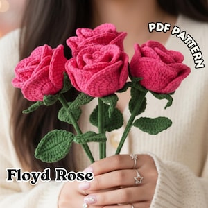 Puede incluir: Primer plano de tres rosas hechas a mano con ganchillo en un vibrante color rosa, con tallos y hojas verdes. El texto "Floyd Rose" está en la parte inferior y "PDF PATTERN" en la parte superior derecha. Las rosas están en manos de una persona.