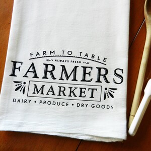 May include: White kitchen towel with black text that reads "Farm to Table Always Fresh Farmers Market Dairy Produce Dry Goods".