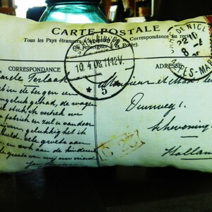 Puede incluir: Una almohada decorativa con un dise&ntilde;o de postal vintage. La almohada presenta un fondo verde descolorido con texto negro y un sello rojo, blanco y azul. El texto en la almohada dice "Carte Postale" y "Correspondance."