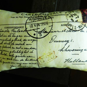 Puede incluir: Una almohada amarilla con un dise&ntilde;o de postal vintage. La postal presenta un sello con el texto "CARTE POSTALE" y un mensaje escrito a mano en alem&aacute;n. La almohada es un gran acento decorativo para un hogar.
