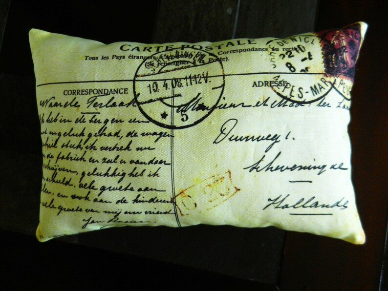 Puede incluir: Una almohada amarilla con un dise&ntilde;o de postal vintage. La postal presenta un sello con el texto "CARTE POSTALE" y un mensaje escrito a mano en alem&aacute;n. La almohada es un gran acento decorativo para un hogar.