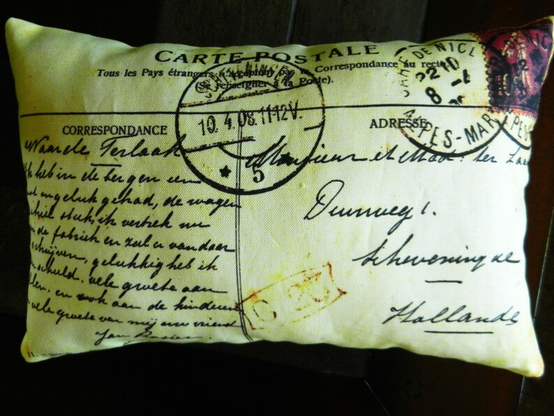 Puede incluir: Una almohada con forma de postal vintage con fondo amarillo y texto negro. El texto incluye las palabras "Carte Postale" y "Correspondance". La almohada tiene un aspecto desgastado y envejecido.