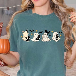 Op de afbeelding: Tealkleurig T-shirt met een Halloween-thema. De afbeelding toont vier cartoongeesten, elk met een zwarte kat, vleermuizen en sterren. Het shirt is een casual stijl, geschikt voor dagelijks gebruik.