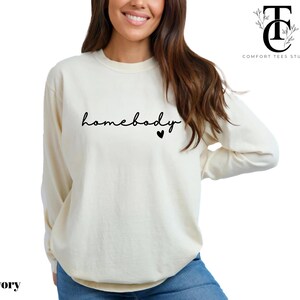 May include: A long-sleeved, ivory-coloured sweatshirt with the text "homebody" in black script and a small black heart.