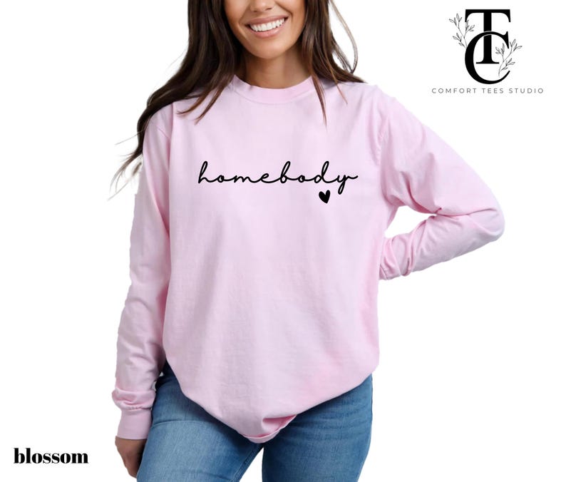 May include: A pink long-sleeved t-shirt with the text "homebody" in black script and a small black heart.