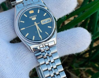 Reloj Seiko 5Automatic 7S26-0070 de acero inoxidable, resistente al agua, con 21 rubíes, día y fecha, fabricado en Japón.