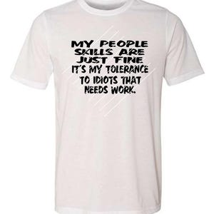 Puede incluir: Camiseta blanca con el texto negro: "MY PEOPLE SKILLS ARE JUST FINE IT'S MY TOLERANCE TO IDIOTS THAT NEEDS WORK." con líneas blancas diagonales. La camiseta tiene cuello redondo y mangas cortas.