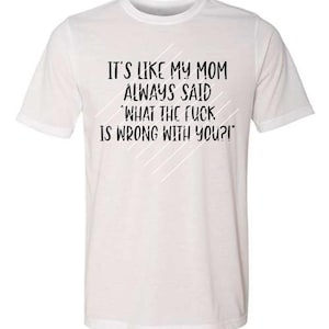 May include: White t-shirt with the text "IT'S LIKE MY MOM ALWAYS SAID 'WHAT THE FUCK IS WRONG WITH YOU?!'" in black. Diagonal white lines are behind the text. The shirt has short sleeves and a crew neck.